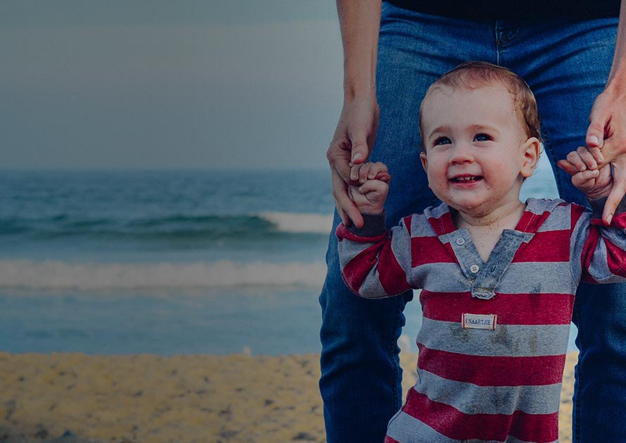 dad helping toddler walk on beach